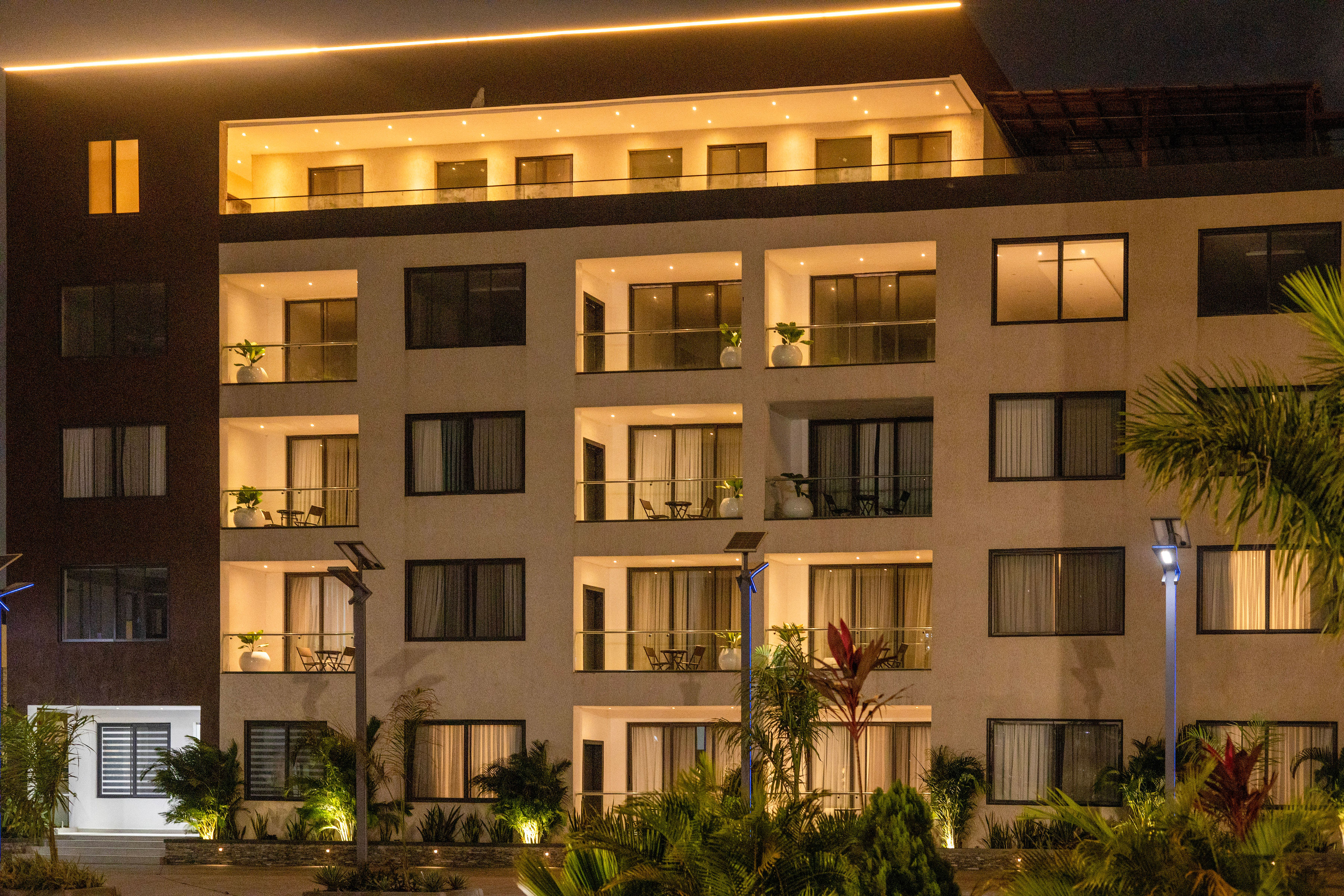 The apartment façade at night, with lit balconies and palms along the courtyard