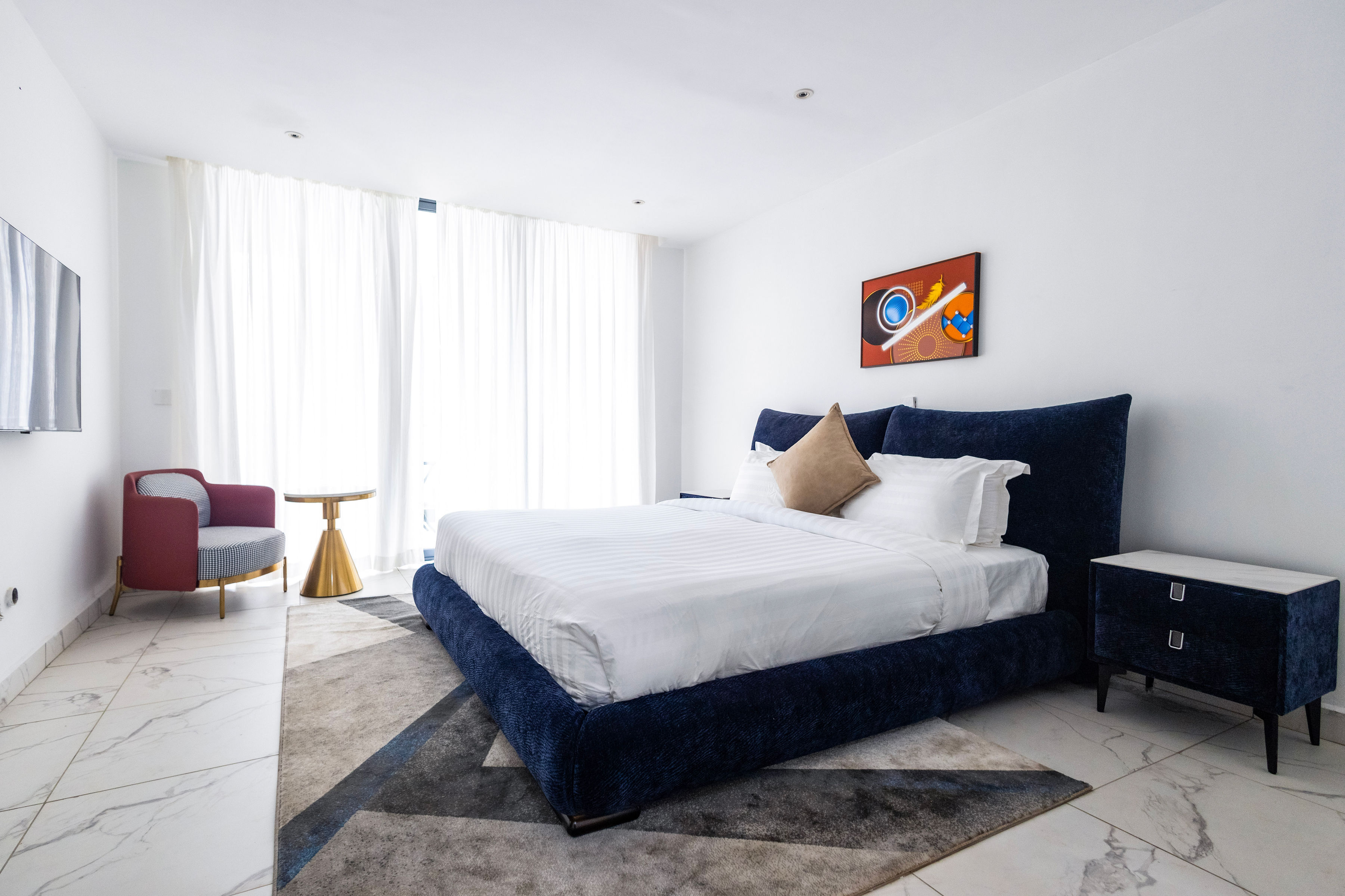 Two-bedroom apartment: bedroom with a navy upholstered bed, armchair and full-height curtains